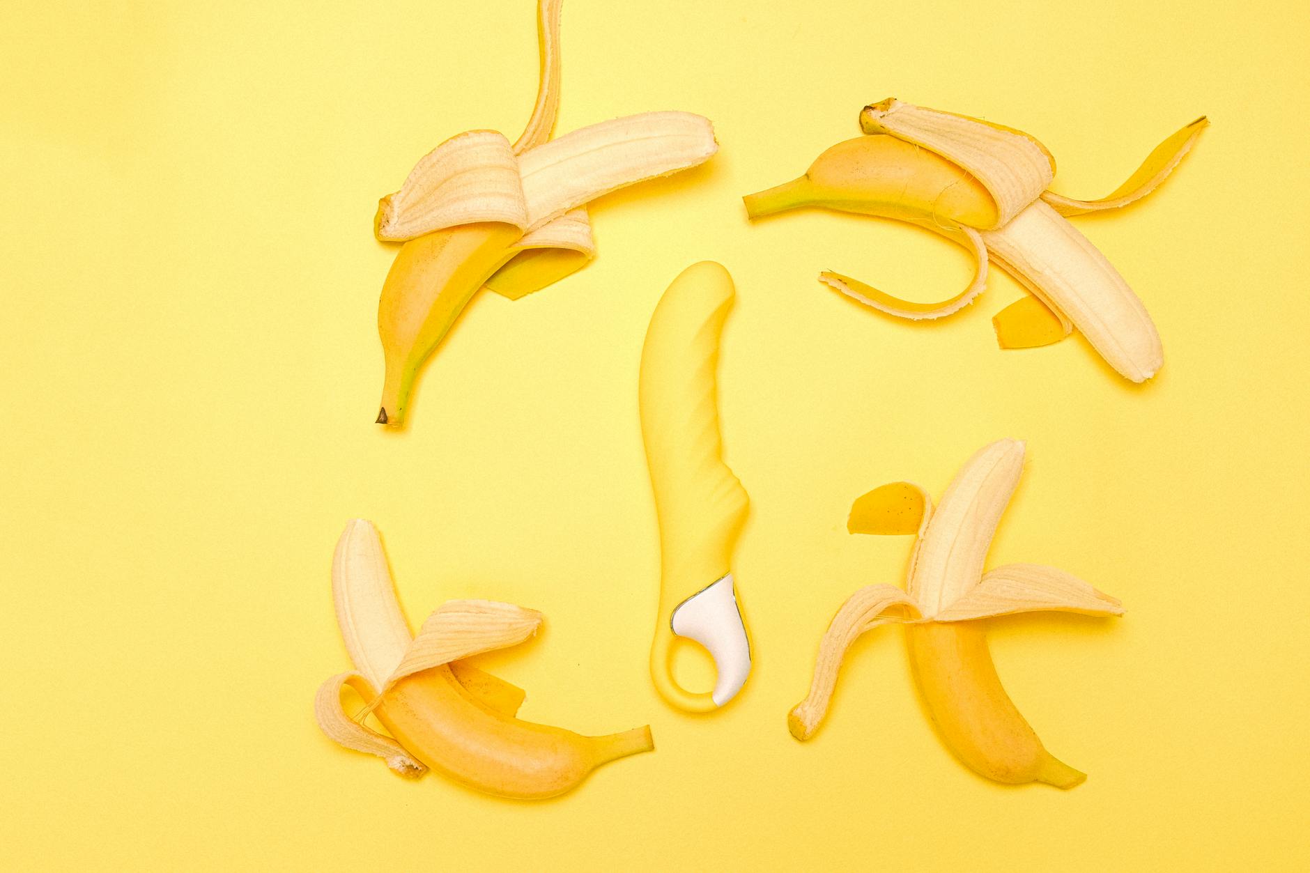 Yellow lemon-shaped vibrator surrounded by fresh lemons on a bright yellow background