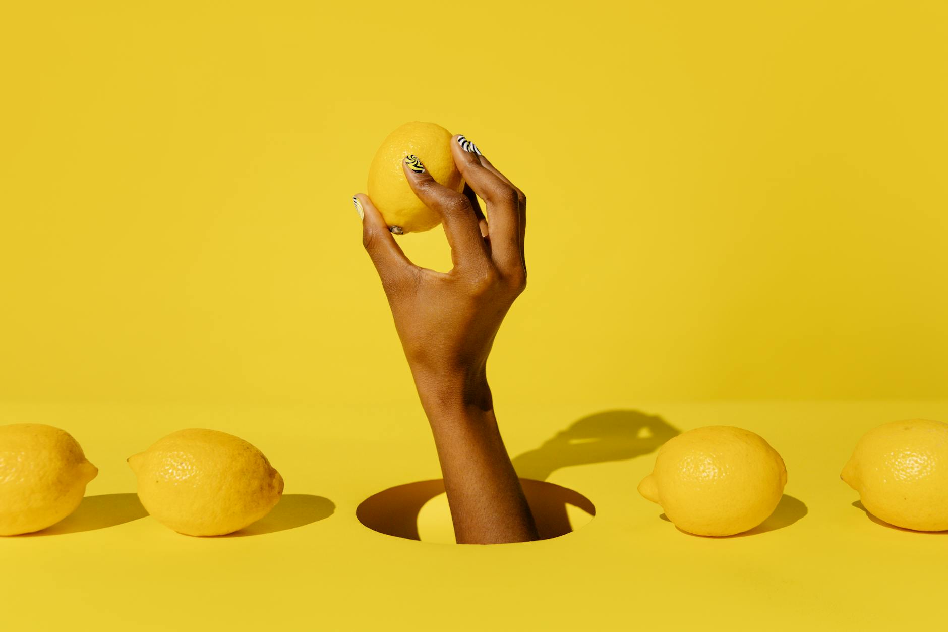 A hand holding a lemon against a vibrant yellow background, symbolizing fresh, natural pleasure
