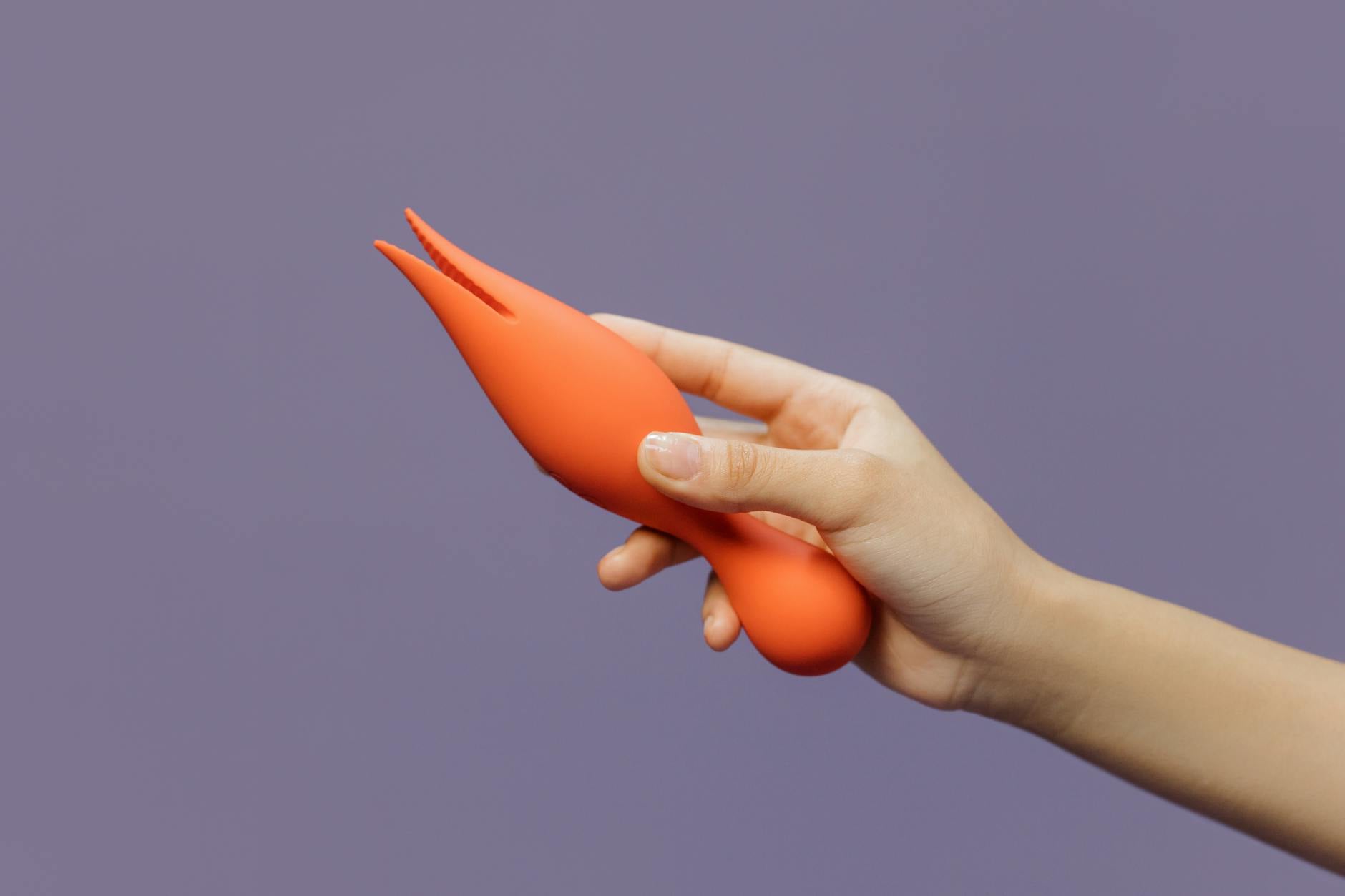 A hand holding a lemon vibrator against a minimalistic purple backdrop, showcasing intimate self-care