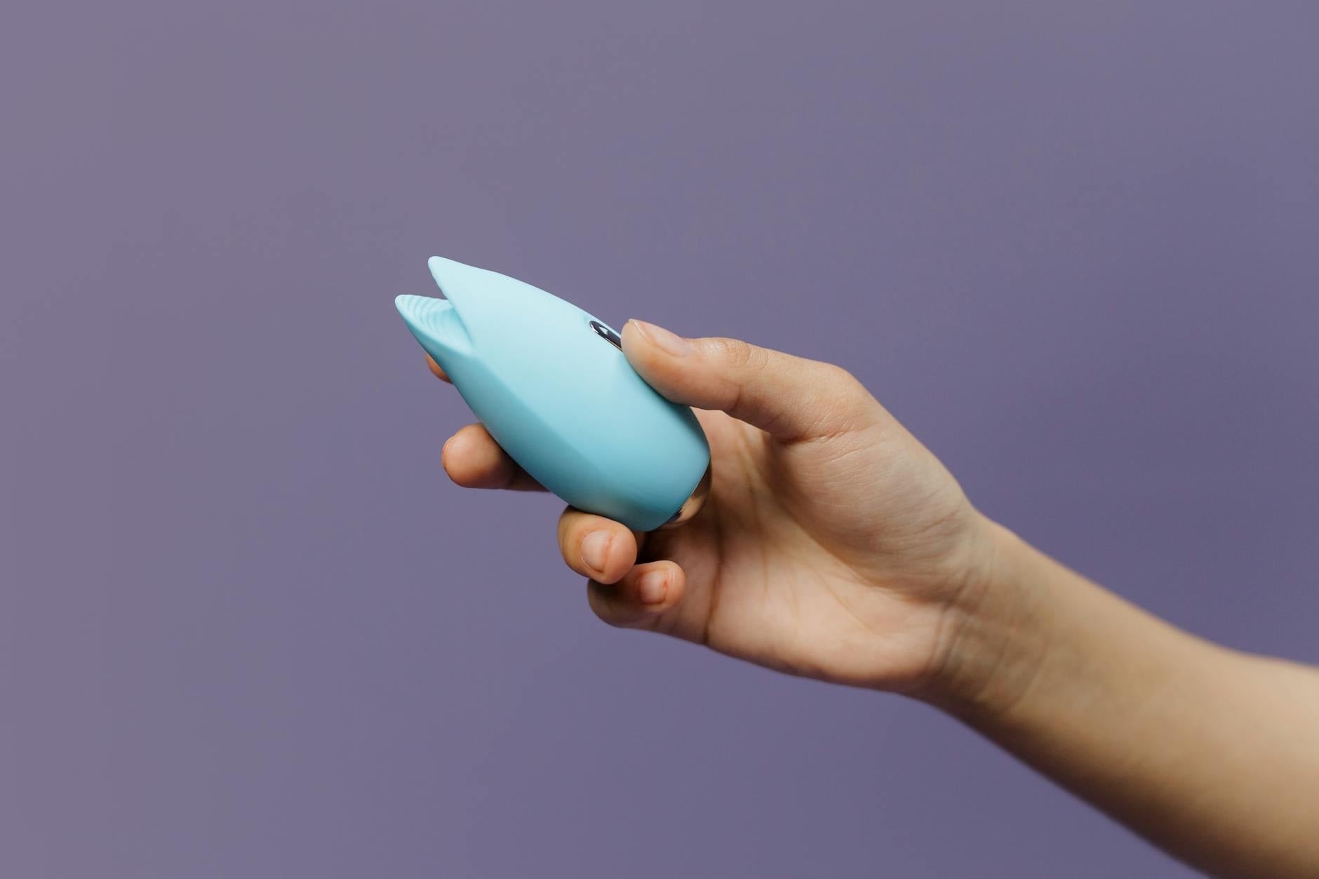 Woman holding blue and pink clitoral vibrators in a thoughtful pose