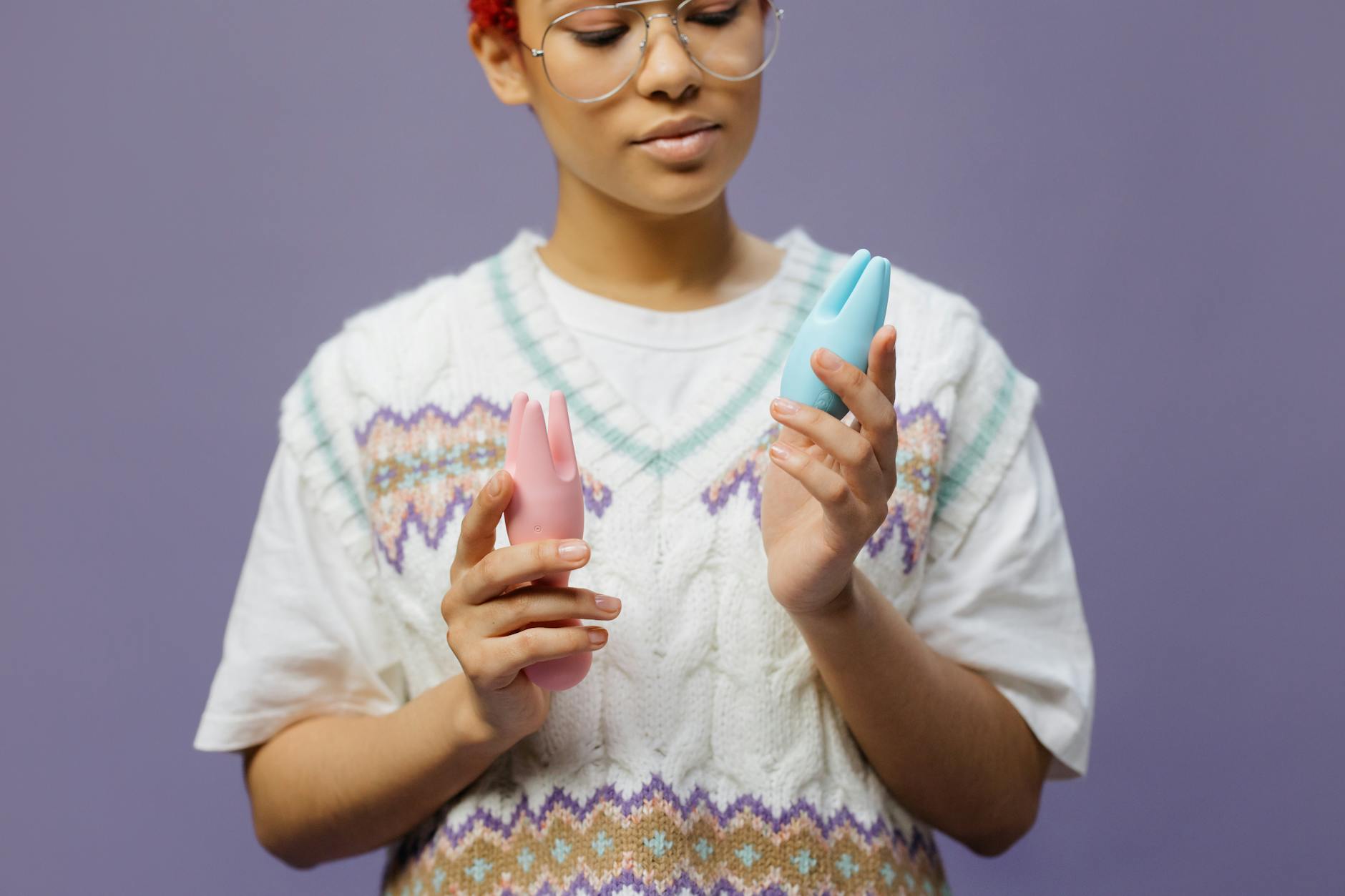 Woman holding blue and pink silicone vibrators in a thoughtful moment